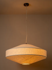A modern pendant light with a wide, shallow conical shade made of textured beige fabric, suspended from a black ceiling canopy by a thin white cord against a warm beige wall. Light turned on.