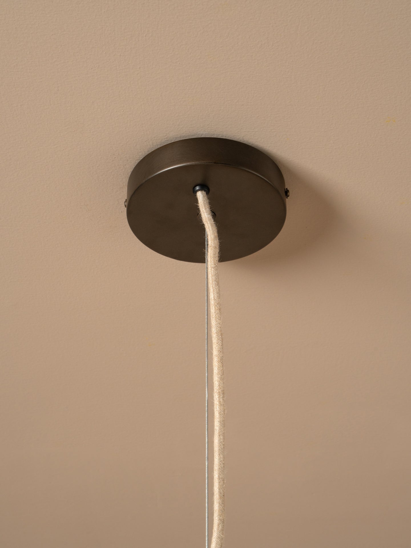 A close-up of a dark metal ceiling canopy with a white fabric cord hanging down against a warm beige wall.