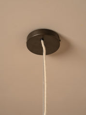 A close-up of a dark metal ceiling canopy with a white fabric cord hanging down against a warm beige wall.