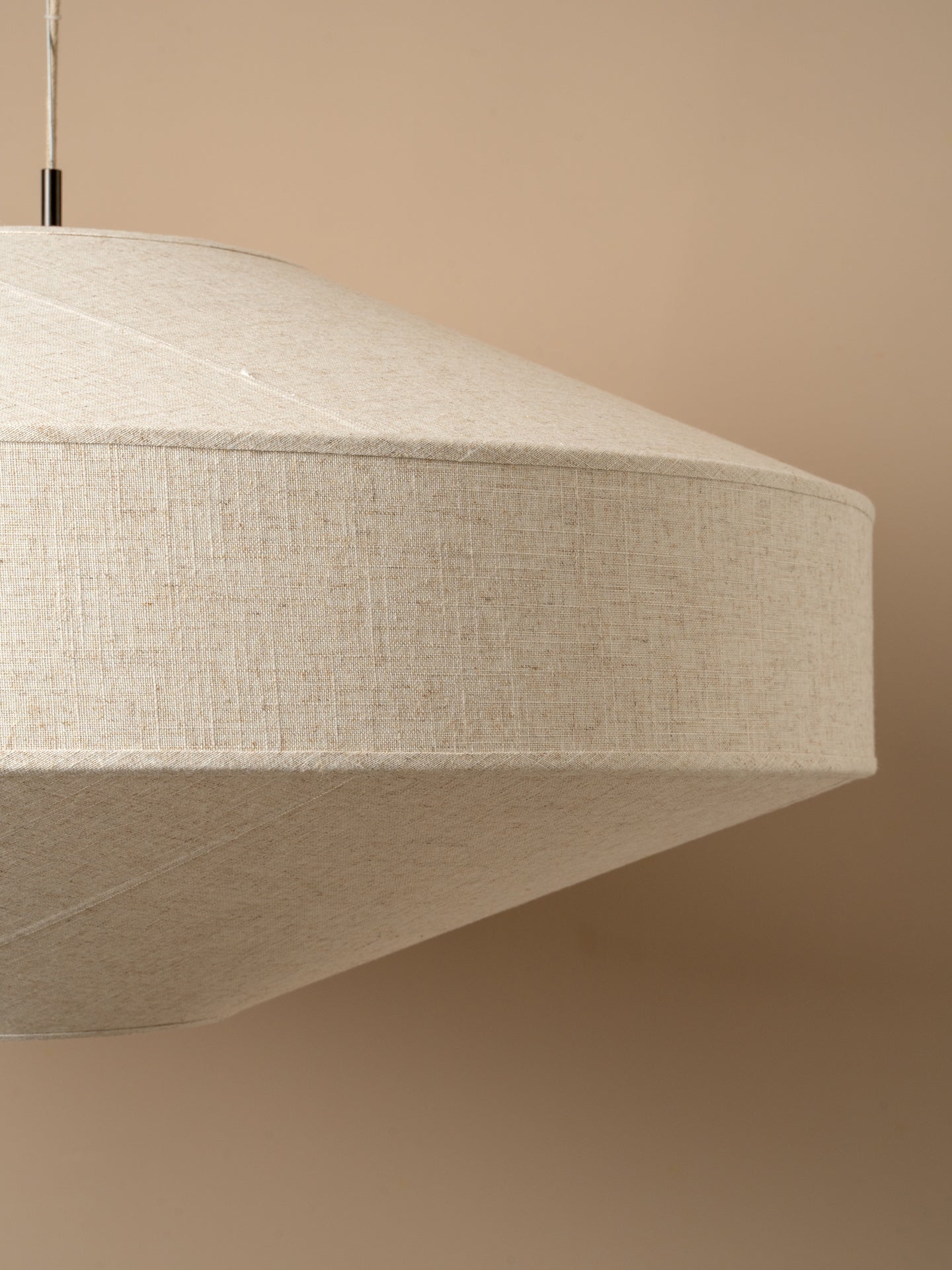 A modern pendant light with a wide, shallow conical shade made of textured beige fabric
