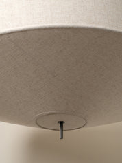 Close-up of the underside of a large drum pendant light shade, showing a textured beige fabric surface and a small black metal canopy fixture.
