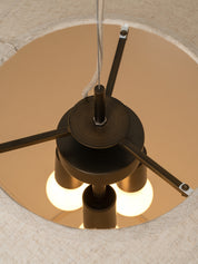 A close-up view from inside a light beige fabric drum shade, showing the top of a three-light ceiling fan with a dark bronze finish and glowing warm white bulbs.