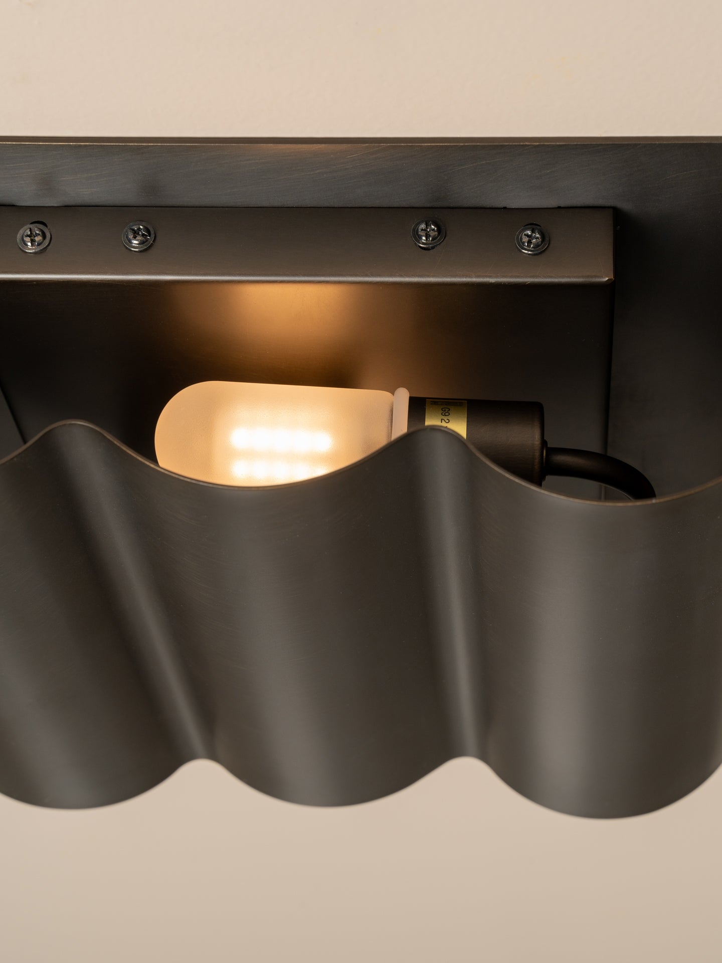 Close-up of a modern wall sconce with a dark charcoal wavy metal shade and a glowing warm light bulb inside.