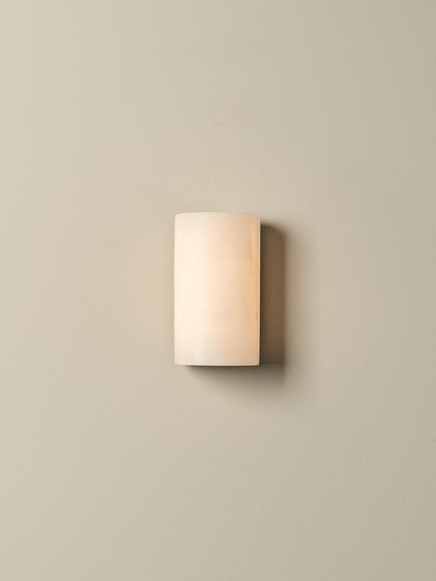 A modern rectangular wall sconce with a frosted, warm-toned glass shade, mounted on a solid beige wall.