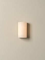 A modern rectangular wall sconce with a frosted, warm-toned glass shade, mounted on a solid beige wall.
