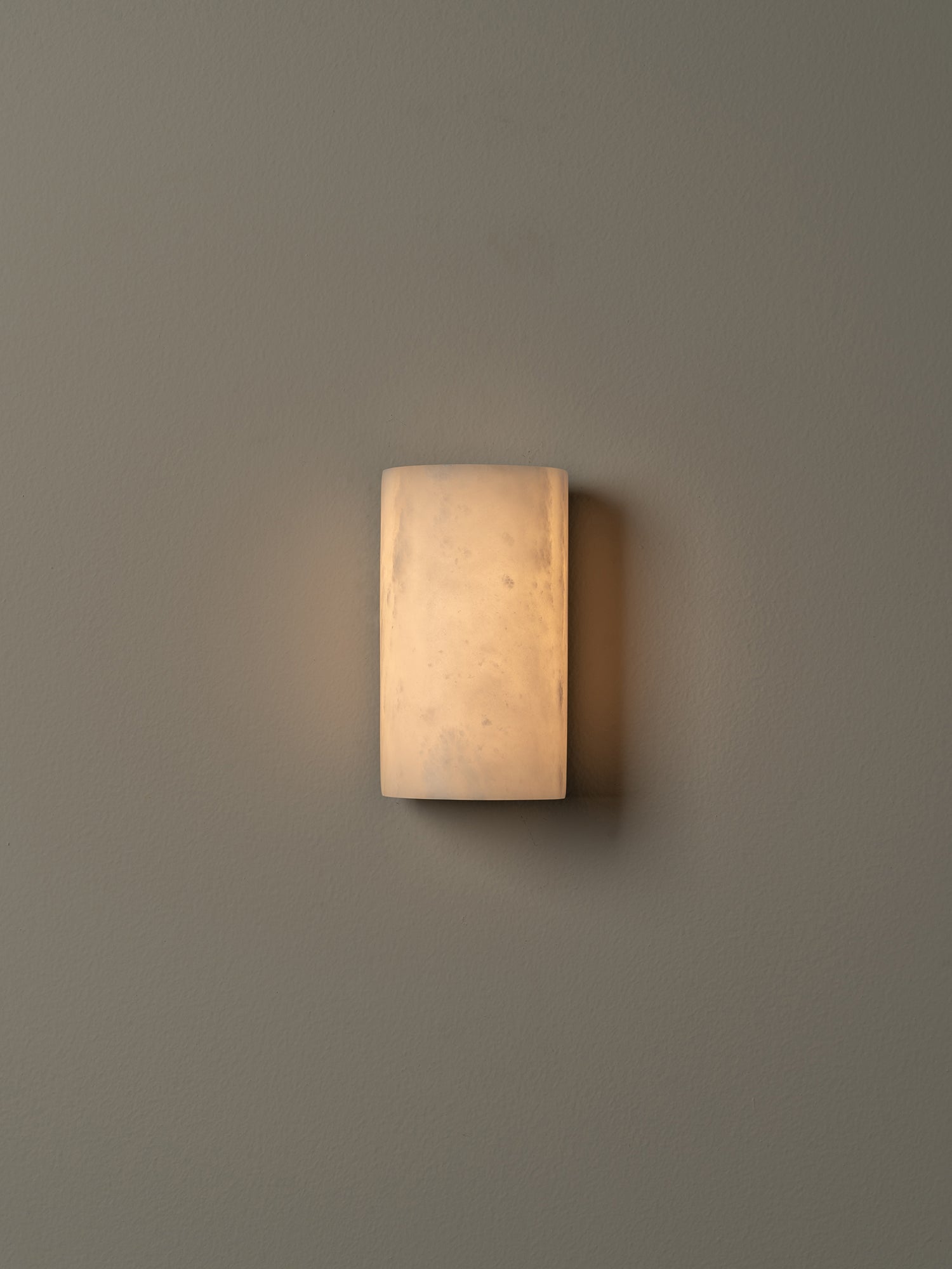 A rectangular wall sconce with a warm, glowing frosted glass shade mounted on a solid gray wall.