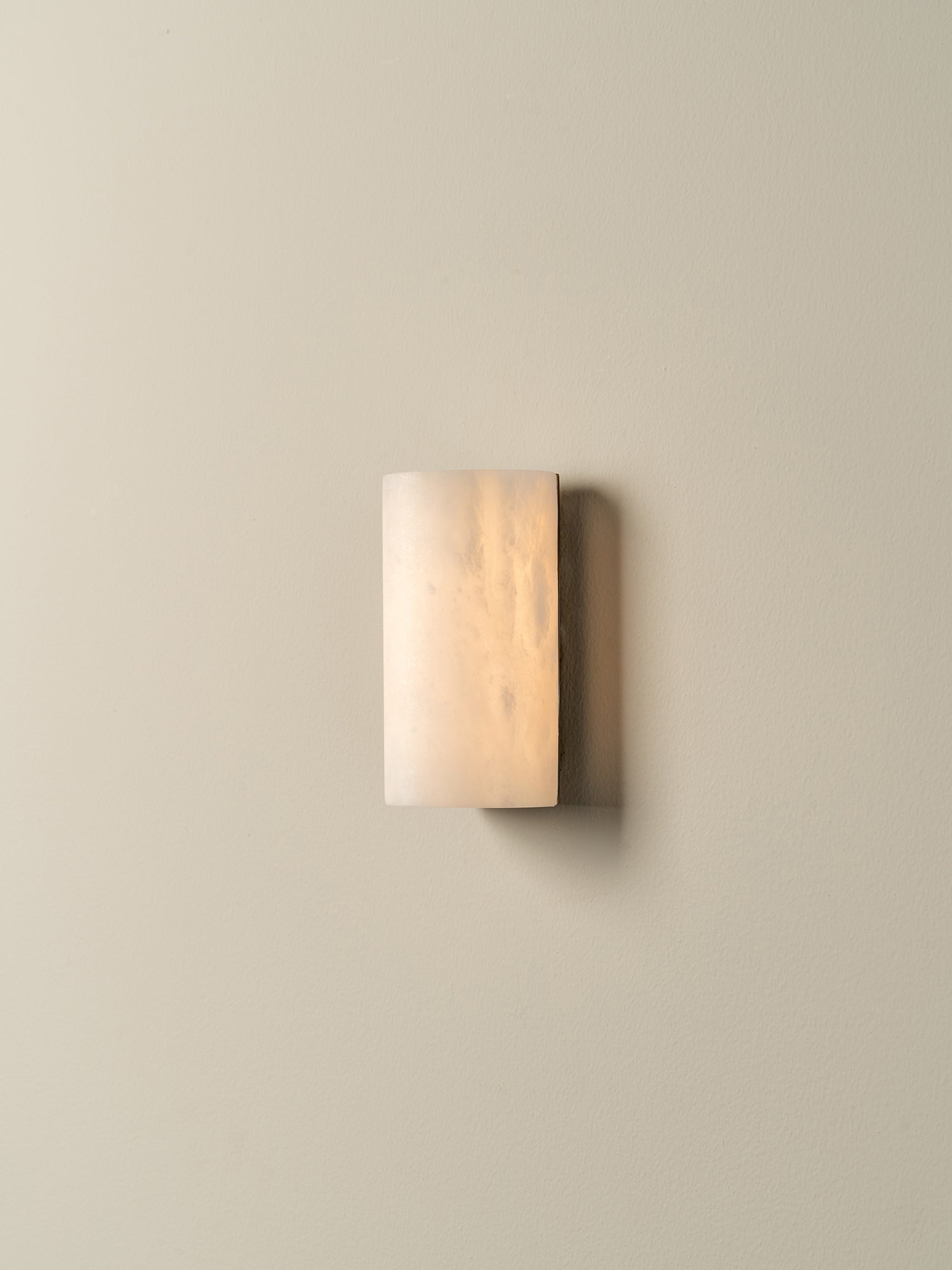A modern rectangular wall sconce with a frosted, warm-toned glass shade, mounted on a solid beige wall.