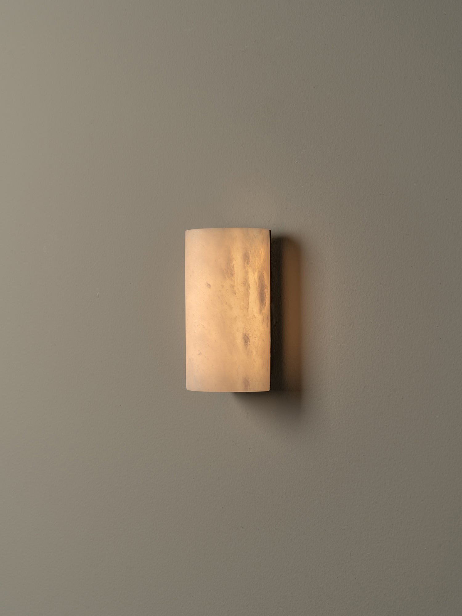 A modern rectangular wall sconce with a frosted, warm-toned glass shade, mounted on a solid beige wall.