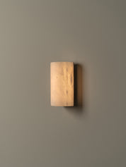 A modern rectangular wall sconce with a frosted, warm-toned glass shade, mounted on a solid beige wall.
