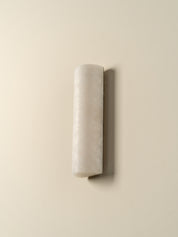 A modern cylindrical wall sconce made of textured off-white stone or marble, mounted on a solid beige wall.