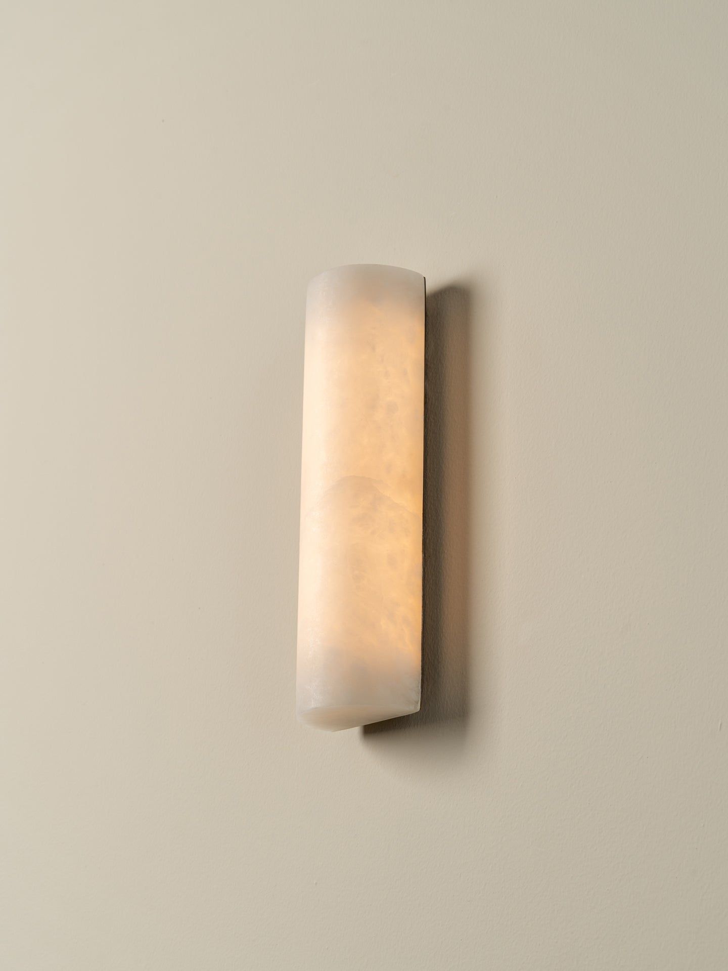A modern vertical rectangular wall sconce with a frosted, textured white glass shade, mounted on a warm beige wall.