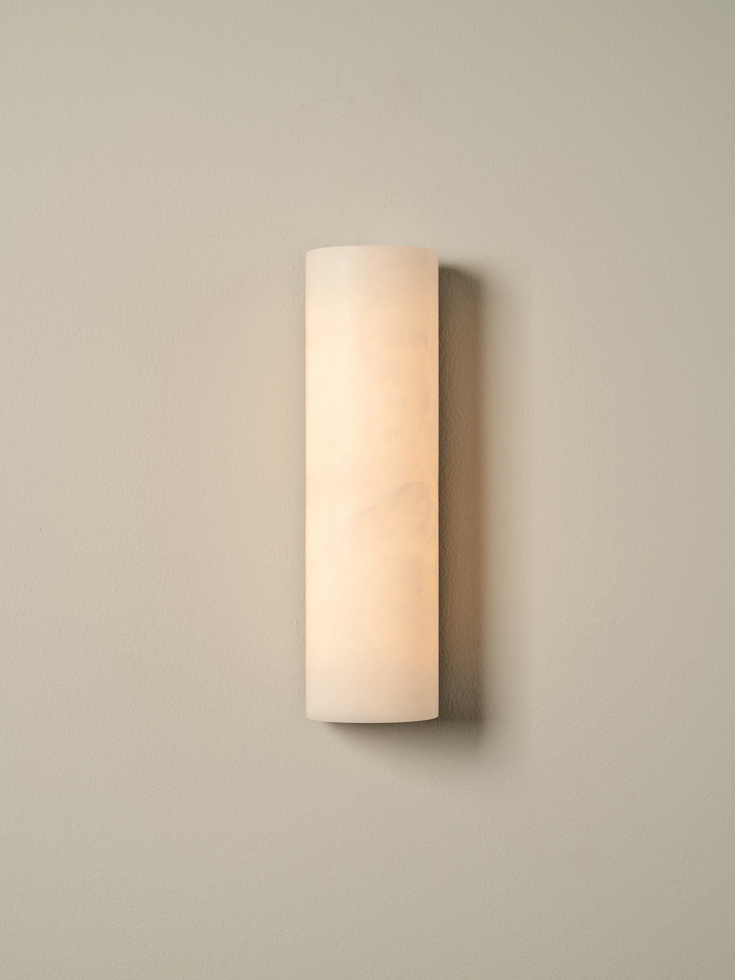 A modern cylindrical wall sconce with a frosted, warm white glass shade, mounted on a neutral beige wall.