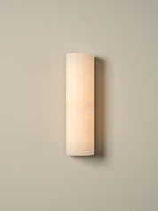 A modern cylindrical wall sconce with a frosted, warm white glass shade, mounted on a neutral beige wall.
