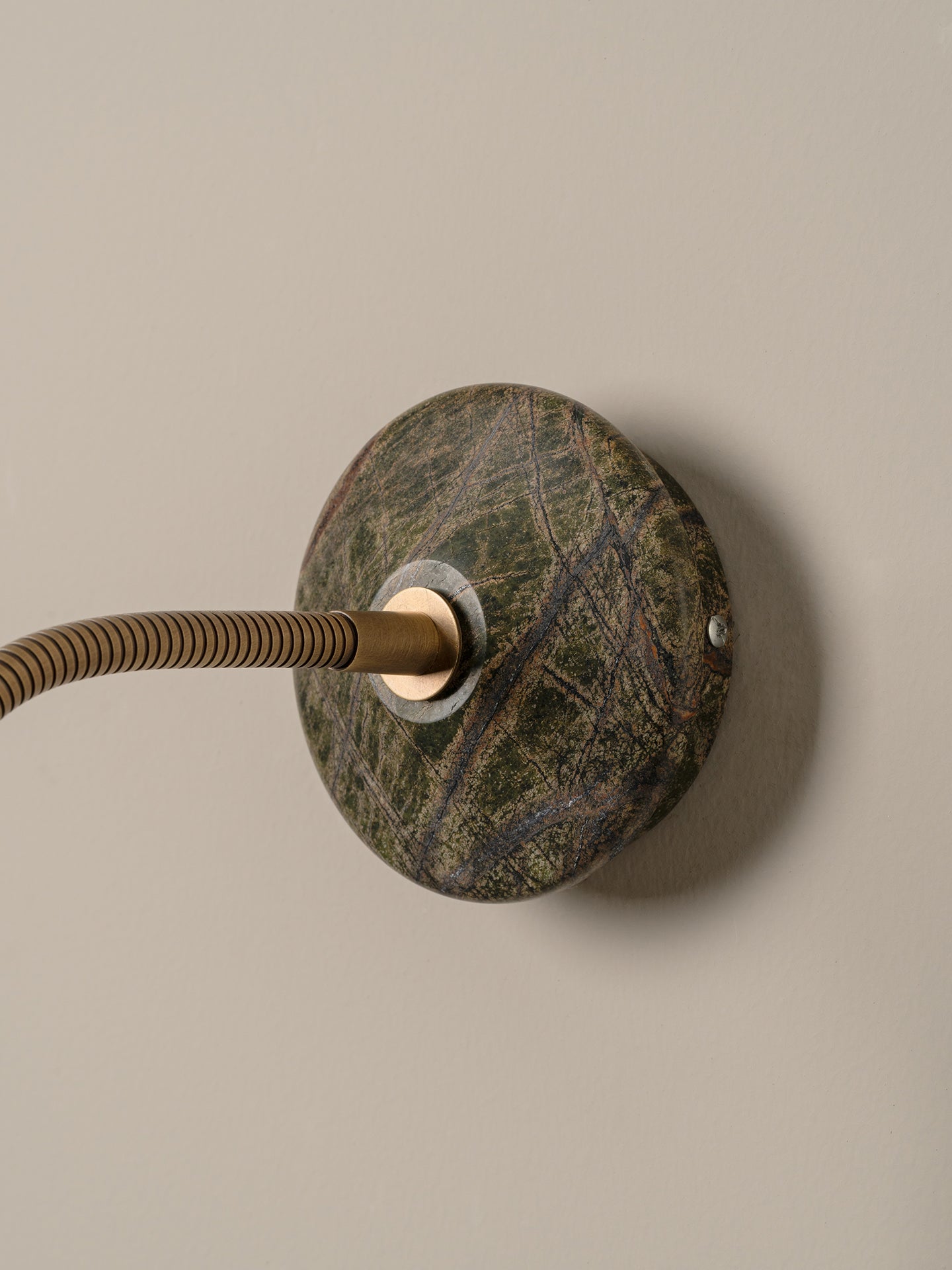 d a round dark green and brown stone backplate, shown against a plain beige wall.