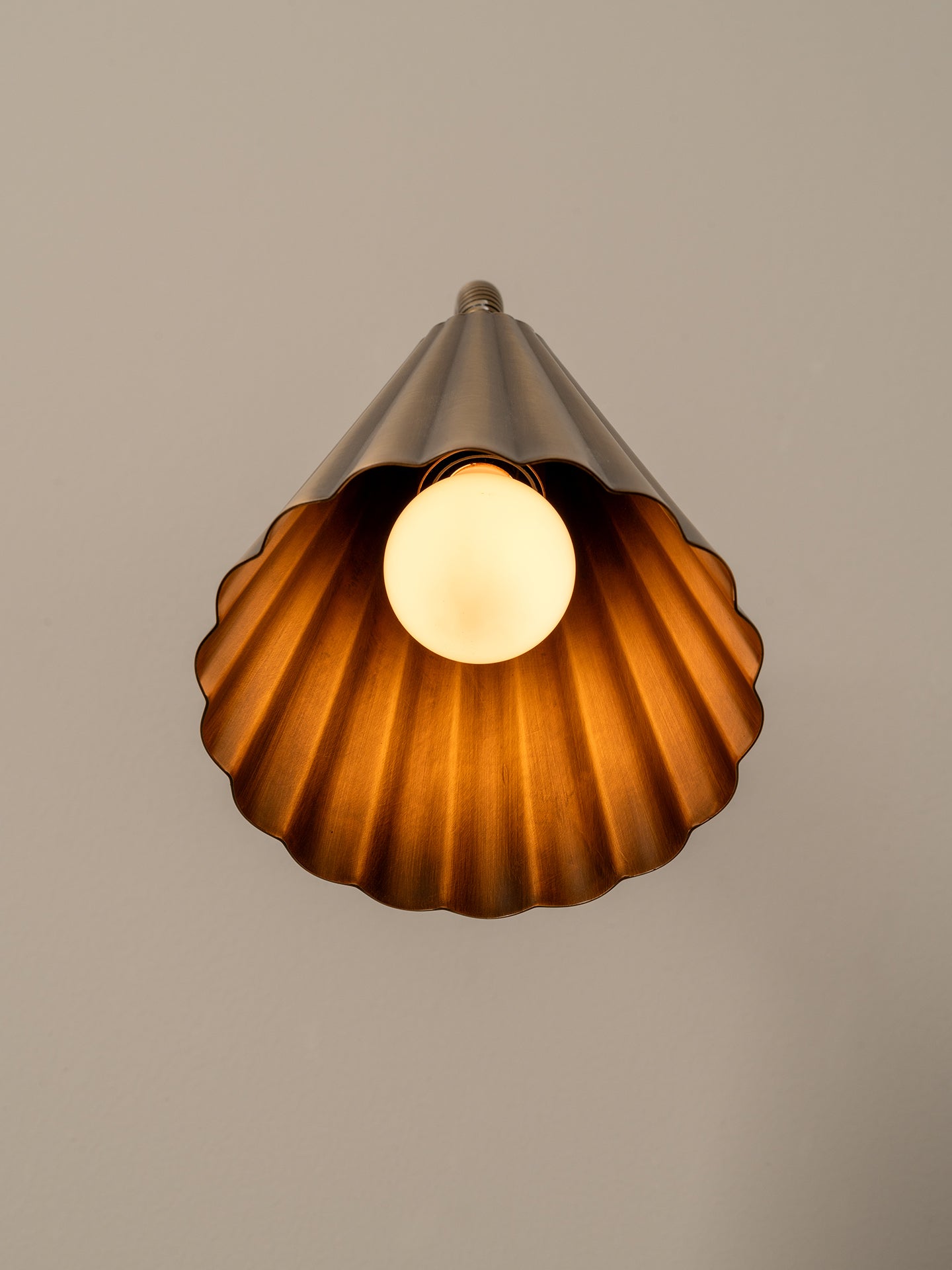 Close up of modern wall-mounted lamp with a fluted brass shade, flexible curved neck, and a round dark green and brown stone backplate, shown against a plain beige wall.