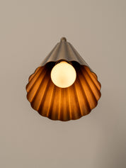 Close up of modern wall-mounted lamp with a fluted brass shade, flexible curved neck, and a round dark green and brown stone backplate, shown against a plain beige wall.