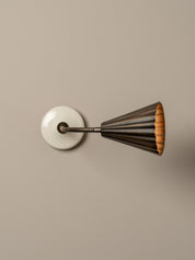 A modern wall sconce with a circular white backplate, a dark metal adjustable arm, and a flared shade featuring a dark bronze exterior and a warm orange-gold interior, mounted on a solid beige wall.