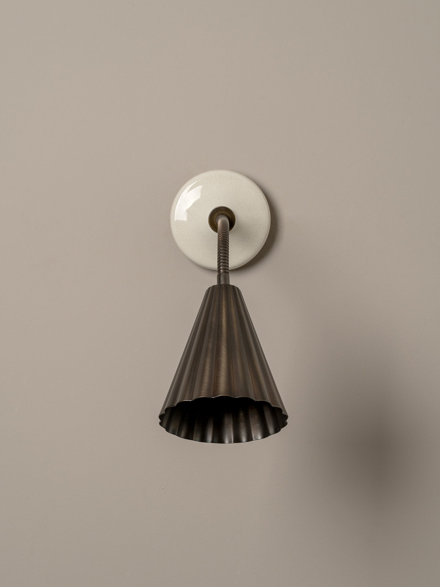 A modern wall-mounted sconce with a fluted dark metal shade and a round white wall plate, shown against a plain warm gray wall.