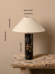 A table lamp with a cream fabric conical shade, a black marble base with gold veining, and overlaid dimension lines showing its height, width, and base width on a rustic wooden table against a beige wall.
