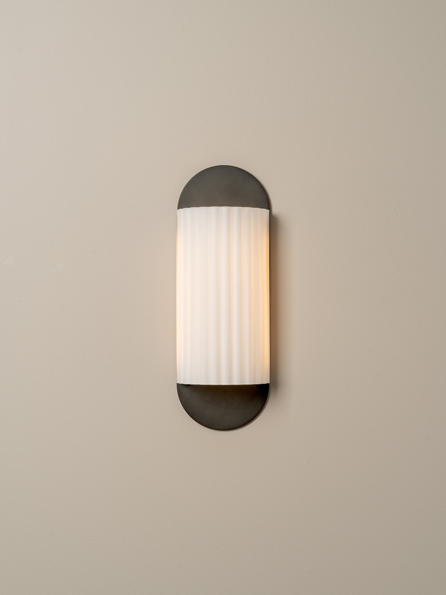 A modern wall sconce light fixture with a vertical ribbed white glass shade and dark charcoal metal caps, mounted on a plain beige wall.