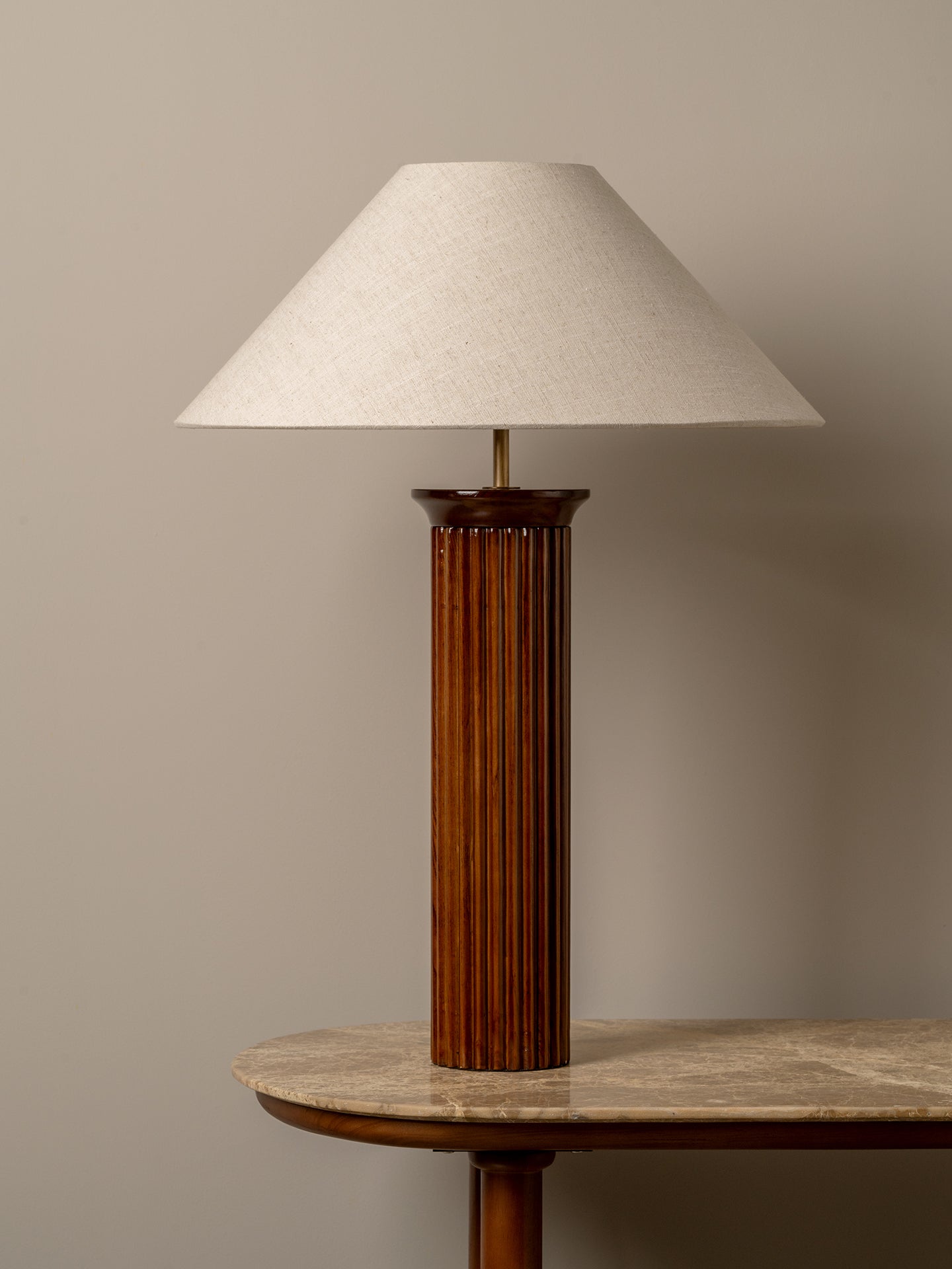 A mid-century modern table lamp with a fluted dark brown wooden column base and a tapered off-white fabric shade, shown on a stone-topped side table against a neutral beige wall.