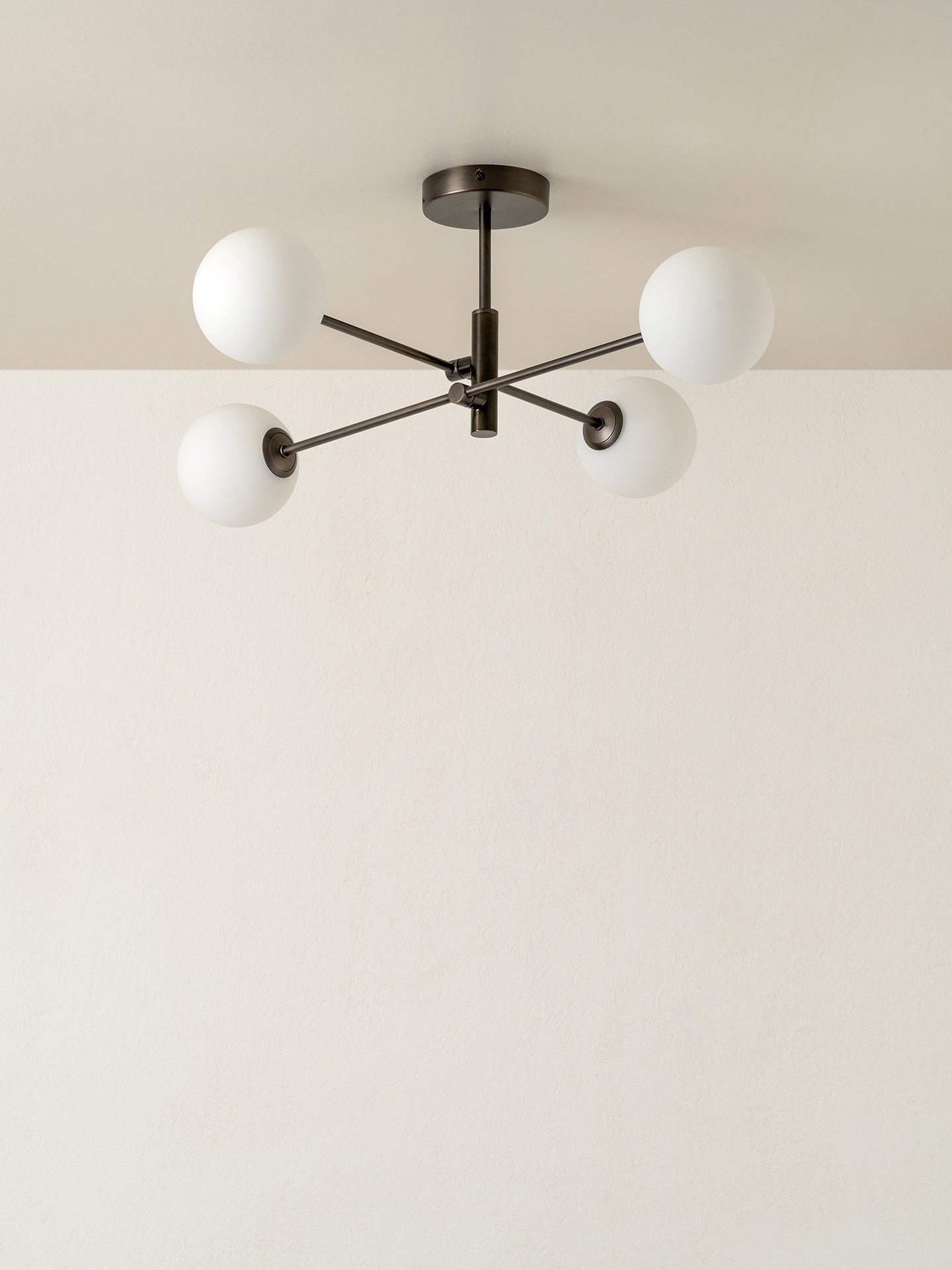 A modern four-light chandelier with frosted white spherical glass shades and a dark metal central frame, shown mounted on a ceiling against a plain off-white wall.