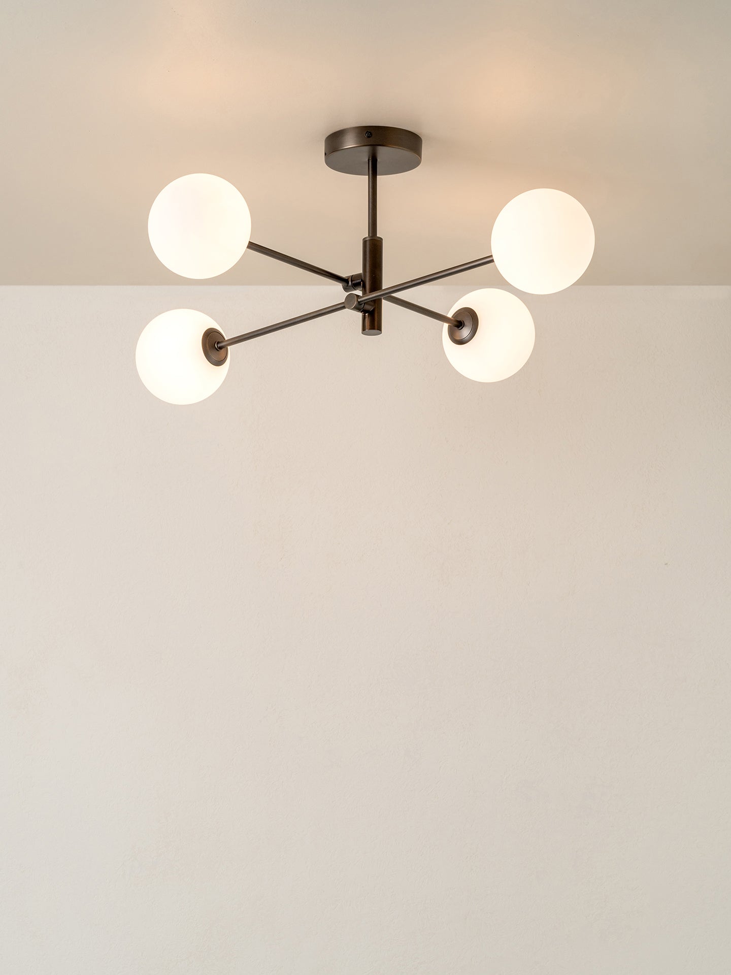 A modern four-light chandelier with frosted white spherical glass shades and a dark metal central frame, shown mounted on a ceiling against a plain off-white wall.