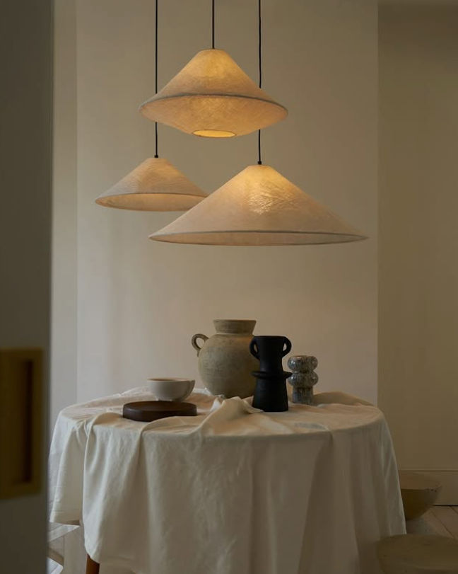 Three cone-shaped pendant lights hanging above a table with ceramic items.